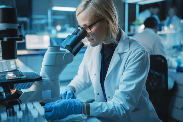 Female Research Scientist is Wearing Glasses and Looking Under the Microscope to Make Analysis of New Biological Samples. Scientists Workingin Modern Laboratory with Help of Modern Technologies.