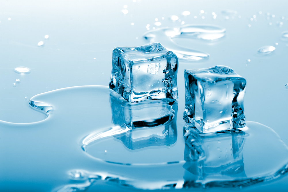 Two azure colored ice cubes melted in water on reflection surface ready to be added to a cocktail